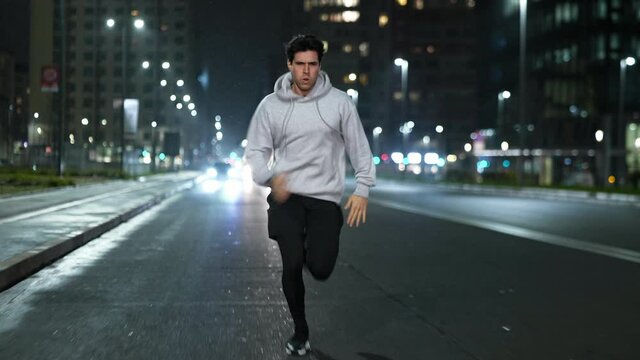 Cinematic shot of young male sportsman with athletic body is running with effort and dedication in city center with snow falling at night. Concept of determination, motivation and goal achievement.