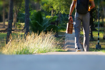 An Asian man in work clothes walks with a lunch box and a meal to go to work in the morning.