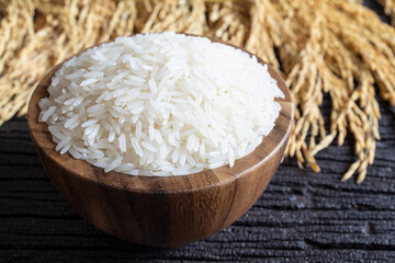 White rice (Thai Jasmine rice) in wooden bowl and paddy rice on dark wooden texture background.