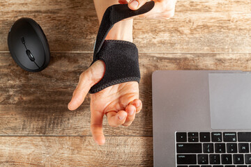 Chronic trauma to the wrist joint  in people using computer mouse may lead to disorders that cause inflammation and pain. A woman working on desk uses wrist support brace and ergonomic vertical mouse