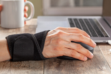 Chronic trauma to the wrist joint  in people using computer mouse may lead to disorders that cause inflammation and pain. A woman working on desk uses wrist support brace and ergonomic vertical mouse