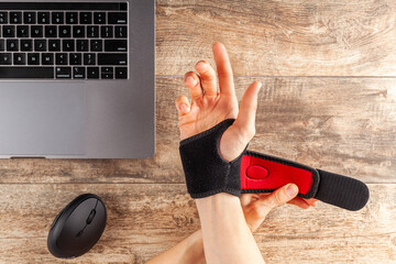 Chronic trauma to the wrist joint  in people using computer mouse may lead to disorders that cause inflammation and pain. A woman working on desk uses wrist support brace and ergonomic vertical mouse