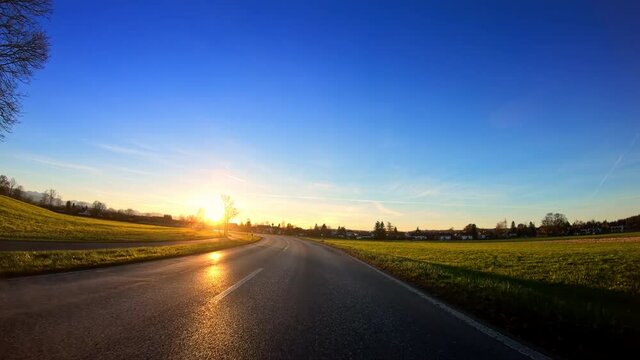Beautiful nature, countryside POV vehicle drive, local asphalt road with sunlight reflection, blue sky and yellow golden shining sun, car travel gopro point of view