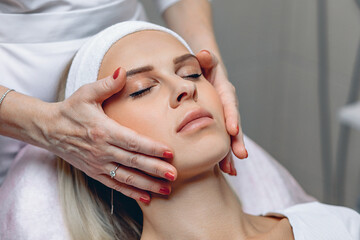 Fototapeta na wymiar Adorable lovely woman enjoying a facial massage in a beauty salon after undergoing cosmetic procedures. Beauty salon concept