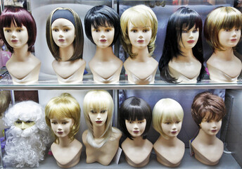 a row of various female wigs on mannequin heads in a shop window 