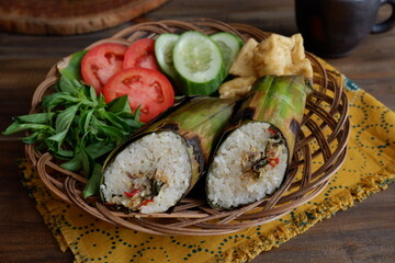 nasi bakar or baked rice with dishes wrapped in leaves served with vegetables in a woven plate on the table