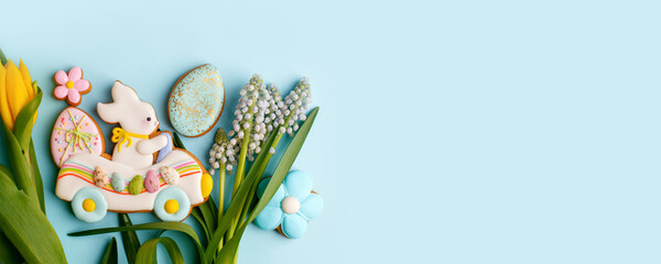 Fototapeta na wymiar Happy Easter. Multi-colored pastel easter cookies gingerbread, seasonal flowers tulips on pastel blue background. Easter concept, copy space, flyer, banner, coupon, greeting card, invitation