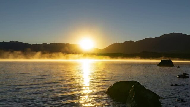 Time-lapse of Lake Tekapo at sunrise, golden sunlight's reflection on water, South Island of New Zealand