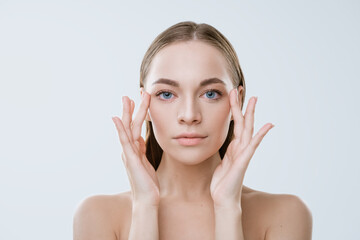 portrait of a young woman with clean skin touches her face with her fingers on a light background