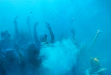 silhouettes of people raising their hands in blue smoke from powdered color dyes, background.