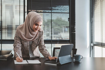 Beautiful asian muslim business woman brown hijab sitting and working with laptop computer at modern office.