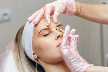 Neat master beautician who injects Botox in the brow area of ​​a beautiful, charming patient. Anti-aging treatment concept