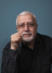 Obraz premium elderly handsome charismatic man sitting in glasses looking at the camera, studio, dark background, portrait