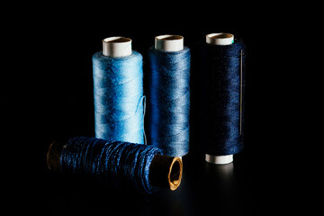 Reel with blue sewing silk threads and needles isolated on a black background, close-up, copy...