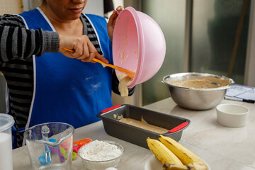 Repostería en casa. Mujer mexicana preparando un panque de plátano, vaciando la masa en el...