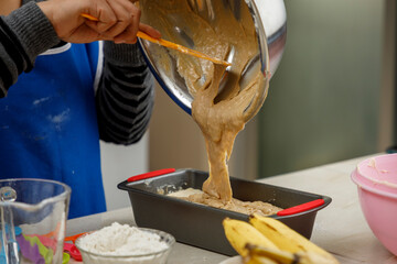 Repostería en casa. Mujer mexicana preparando un panque de plátano, vaciando la masa en el...