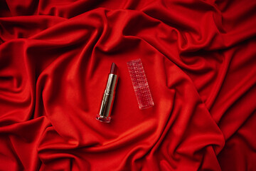 Red lipstick lies on the fabric. Red fabric in a nice fold close-up.