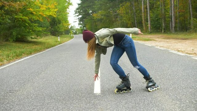Young girl with inline skates on the street, having fun doing a handstand. Road in the forest during the autumn day.