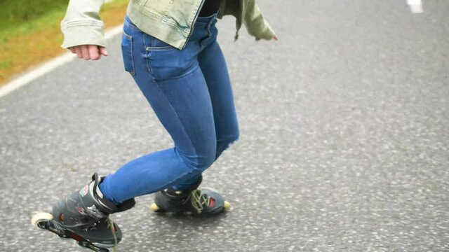 Young girl with inline skates on the street, is skating backwards. Road in the forest during the autumn day.