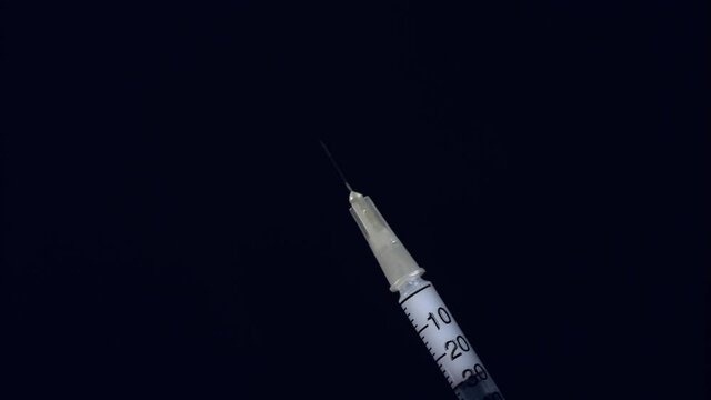 Flicking a full hypodermic needle to release air bubbles. Close up shot, isolated black background