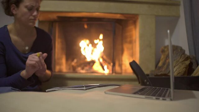 Caucasian woman relaxing by the fireplace, colouring pages at home. Medium pan shot.