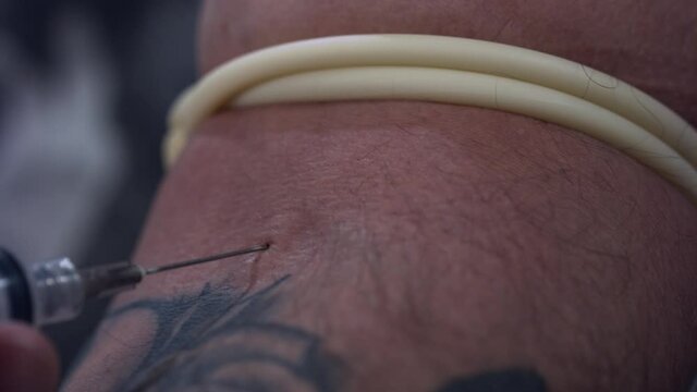 Macro shot of a hypodermic needle sticking into an adult male's forearm veins.