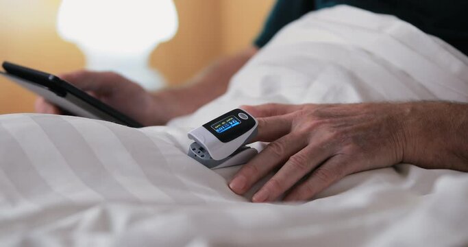 Pensioner use digital reader electronic book and check oxygen saturation and heart rate with pulse oximeter. Modern technologies for home health protection. Safe life with modern digital device.