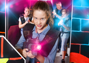Emotional teen girl with a laser pistol playing laser tag with family on dark labyrinth