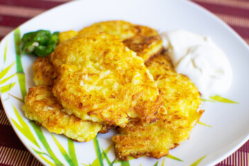 Appetizing zucchini pancakes with herbs on a white plate on the table.