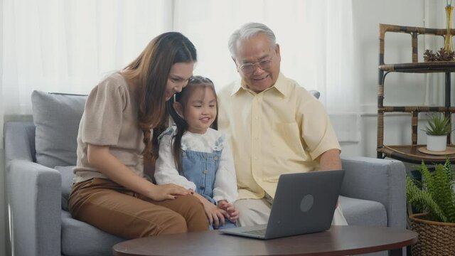 Happy family senior grandfather, daughter and granddaughter talking online via video chat using laptop computer with father, old grandpa embracing little grand child and mother in living room at home