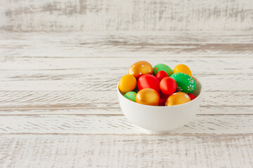 Colorful hand painted easter eggs in white ceramic bowl on wooden table with copy space.