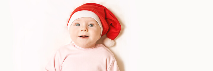 Cute small boy lying at bed. Childhood christmas concept. Light background. Smiling child. Xmas red hat. Copyspace. Stay home. Mockup. Horizontal banner. Pink female clothes