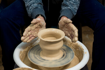 Fototapeta na wymiar The woman potter's hands formed by a clay pot on a potter's wheel. The potter works in a workshop