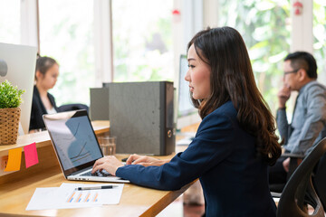 Asian businesswoman using laptop computer co-working with her team in a busy business corporate modern office. workspace and shared office, diverse women coworkers and office together concept