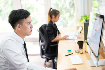 Obraz premium Asian businessman using desktop computer co-working with team in a busy business corporate modern office. workspace and shared office, diversity coworkers and office together concept