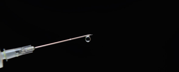 On a black background, a needle from a syringe with a drop on the end. Concept-vaccination of the population. Copy space