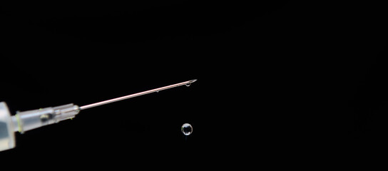 On a black background, a needle from a syringe with a drop on the end. Concept-vaccination of the population. Copy space