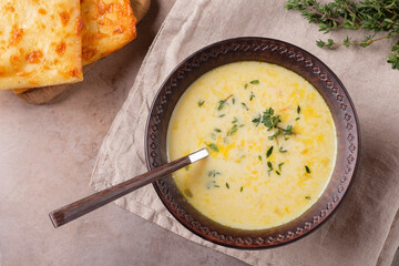 A bowl of cheese soup with thyme and bread on a beige background. Vegetarian food. Top view.
