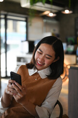 Portrait of cheerful young woman browsing surfing wireless internet on smartphone while sitting in cafe.