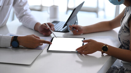 Cropped shot of business people wearing protective mask working on their project with digital tablet at modern office.