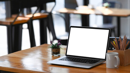 Open computer laptop with empty screen, coffee cup, plant and stationery on wooden table.