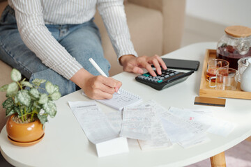 Hands of young woman managing monthly expenses, she is checking bills and writing down figres