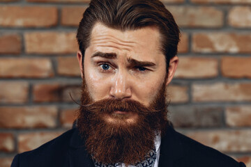 Close up portrait of emotional attractive man with hussar mustache and beard posing against a brick...