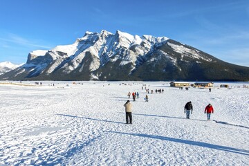 People Walking on Snowy Frozen Lake Minnewanka near Banff on a Sunny but Cold Family Day in Canadian Rocky Mountains
