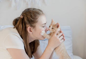 The teenage girl holds a small red kitten and presses it to the face. The concept is the love of pets.