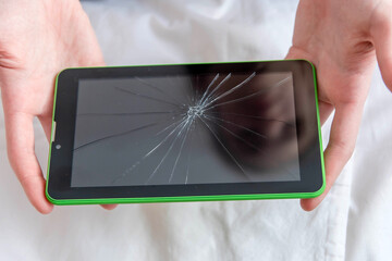 Women's hands hold a tablet with a broken screen.