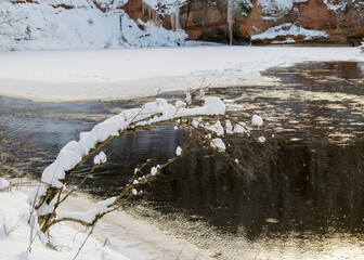Scenic and impressive up to 600 m long and 21 m high outcrop on the river bank. The snow is covered by a river and a rock. It consists of reddish-brown sandstone outcrops of the Gauja suite.