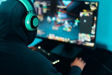 The gamer sitting on a gaming chair and playing computer games. The player has turquoise headphones on his head © Anastassiya 