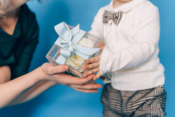 Little boy gives mom a box with a gift against a blue background. Gift for womens day and mothers day.