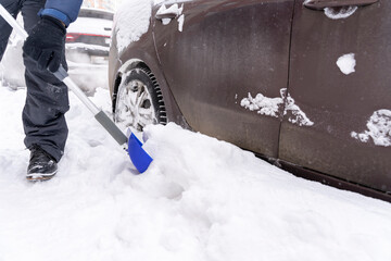 a man digs up his car with a shovel from a snow captivity in a snowfall